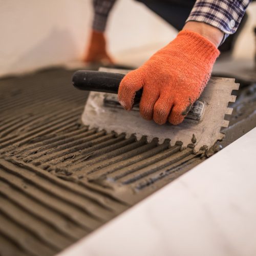 Laying Ceramic Tiles. Troweling mortar onto a concrete floor in preparation for laying white floor tile. Troweling mortar onto a concrete floor in preparation for laying white floor tile.
